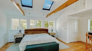 A bedroom with a large bed, skylights, a wooden ceiling, and a view of trees through the windows. - Lakefront house on Damariscotta Lake, perfect getaway (Nobleboro)