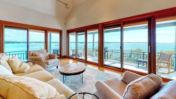 A spacious living room with large windows, a sofa, a coffee table, and a view of the sea. - Delightful oceanfront home with amazing views, wrap-around deck & two fireplaces (Westport)