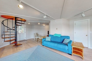 A modern living room with a blue sofa, a spiral staircase, and a dining area.