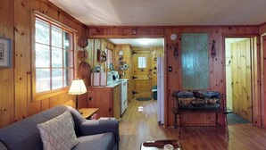 A wooden interior with a sofa, a bench, a lamp, and a kitchen area. - Lakefront cabin with private dock & beach access (Greenville)