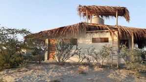 Un bâtiment à toit de chaume, doté d’un réservoir d’eau cylindrique, entouré d’une végétation clairsemée.