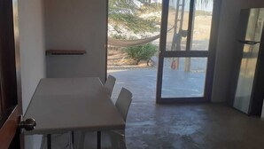 Une pièce avec une table blanche, des chaises, une porte donnant sur l’extérieur et une petite étagère.