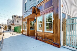 A two-story building with a wooden front porch, large windows, and a visible garage door. - Cozy & Clean Second-Story Suite w/ Kitchenette & Free WiFi - Walk to the Harbor (Northeast Harbor)