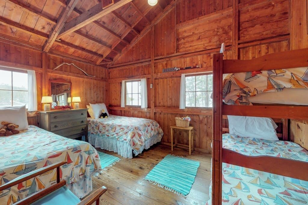Una cabaña con paredes de madera, una litera, un escritorio con lámpara y una cama con colcha estampada.