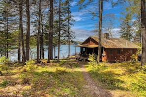 A cabin with a porch, surrounded by tall trees and a lake.