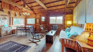 Ein rustikales Blockhaus-Interieur mit Holzwänden, einem Essbereich, einer Couch, Schaukelstühlen und einer Lampe.