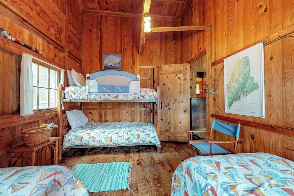Una cabaña con paredes de madera, una cama individual, un escritorio, una silla y un mapa en la pared.