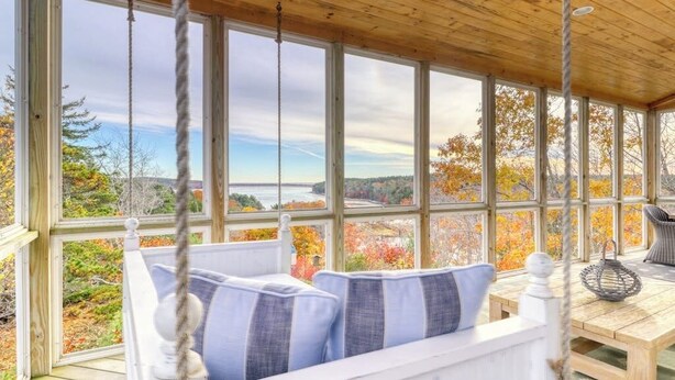 A covered porch with a view of autumn foliage and a body of water.