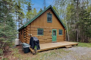 A log cabin with a green door, two windows, a covered deck, and a water tank. - Lakefront home w/ pristine views Outdoor firepit and full kitchen (Greenville)