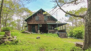 Un chalet rustique avec une porte verte, une véranda et un escalier en pierre menant à l’entrée.