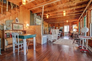 A wooden cabin interior with a dining area, bookshelves, and a staircase. - Historic Home with Large Deck, Free WiFi, Washer/Dryer - Near Beach and Downtown (Boothbay Harbor)