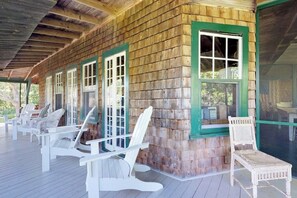Une cabane en bois dotée d’une véranda, de chaises Adirondack blanches et d’une grande fenêtre.