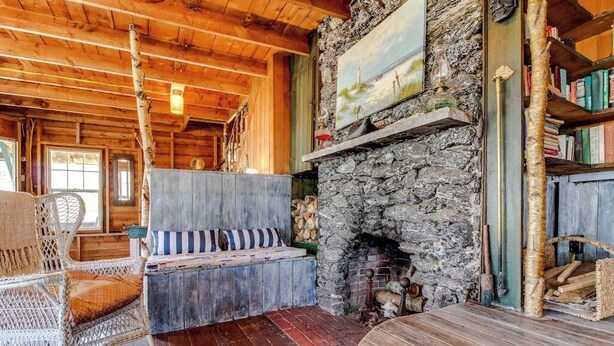 L’intérieur d’un chalet rustique, avec une cheminée en pierre, des poutres en bois au plafond, des meubles en osier et une bibliothèque.