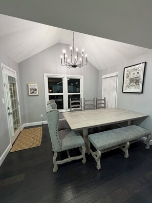 Une salle à manger avec une table en bois, des chaises rembourrées, un lustre et un tableau encadré au mur.