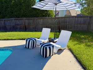 Un jardin avec une piscine, deux chaises longues et un parasol à rayures.