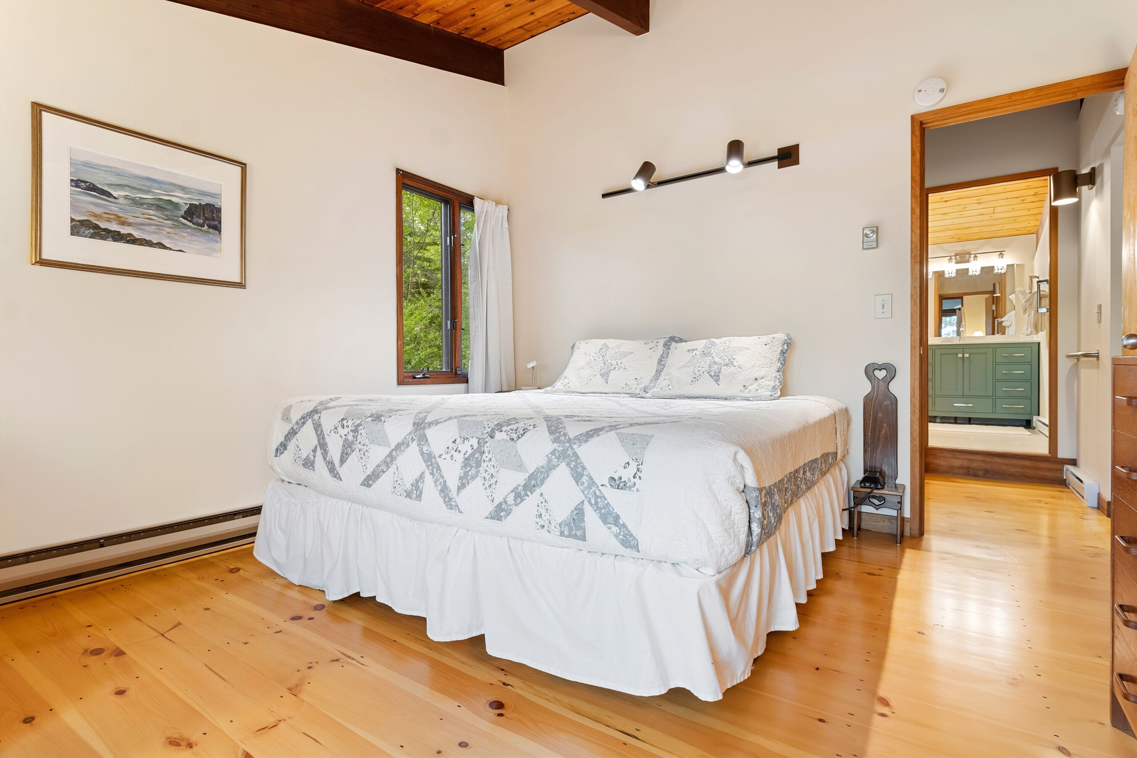 Een slaapkamer met een bed, een raam, een ingelijste foto en een gang naar een badkamer.