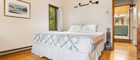 Een slaapkamer met een bed, een raam, een ingelijste foto en een gang naar een badkamer.