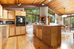 Een houten keuken met een centraal eiland, inbouwapparatuur en grote ramen met uitzicht op de omgeving.