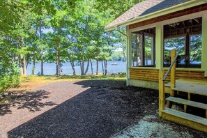 Een houten hut met een veranda met uitzicht op een meer, omringd door bomen.