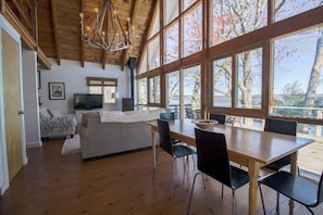 A spacious room with a wooden ceiling, large windows, a dining table with chairs, a sofa, and a television.