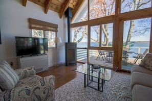 A living room with a television, fireplace, and large windows overlooking a deck.