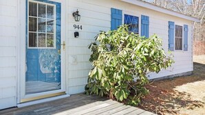 Un bâtiment blanc avec des volets bleus, le numéro « 944 » sur la porte et une terrasse en bois.