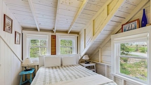 A bedroom with a bed, two windows, a lamp, and a view of greenery.