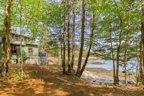 A cabin with a dirt path leading to a body of water, surrounded by trees.