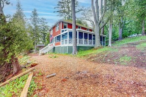 A two-story house with a porch, surrounded by trees and a wooded area.