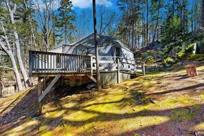 A cabin with a wooden deck and stairs leading up to it, surrounded by trees and a forested area.