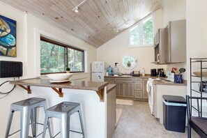 A kitchen with a central island, bar stools, a refrigerator, and a window overlooking greenery.