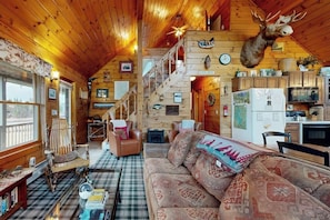 Ein rustikaler Innenraum einer Blockhütte mit Treppe, montiertem Elchgeweih, einer Couch und einem Esstisch.