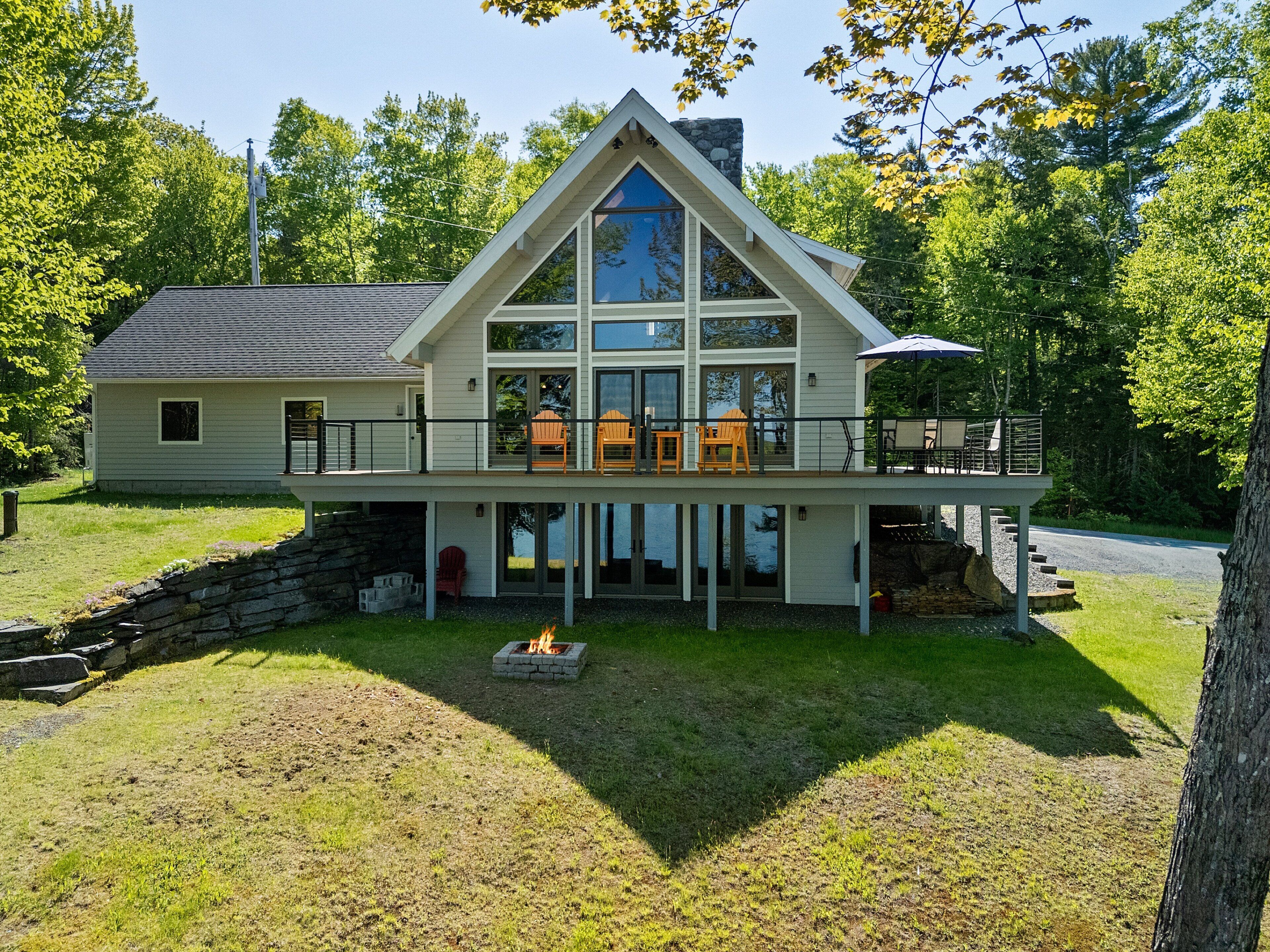 A two-story house with a large balcony, a stone fireplace, and a view of the surrounding trees.
