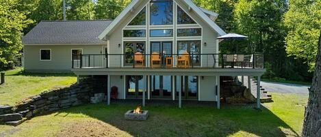 A two-story house with a large balcony, a stone fireplace, and a view of the surrounding trees.