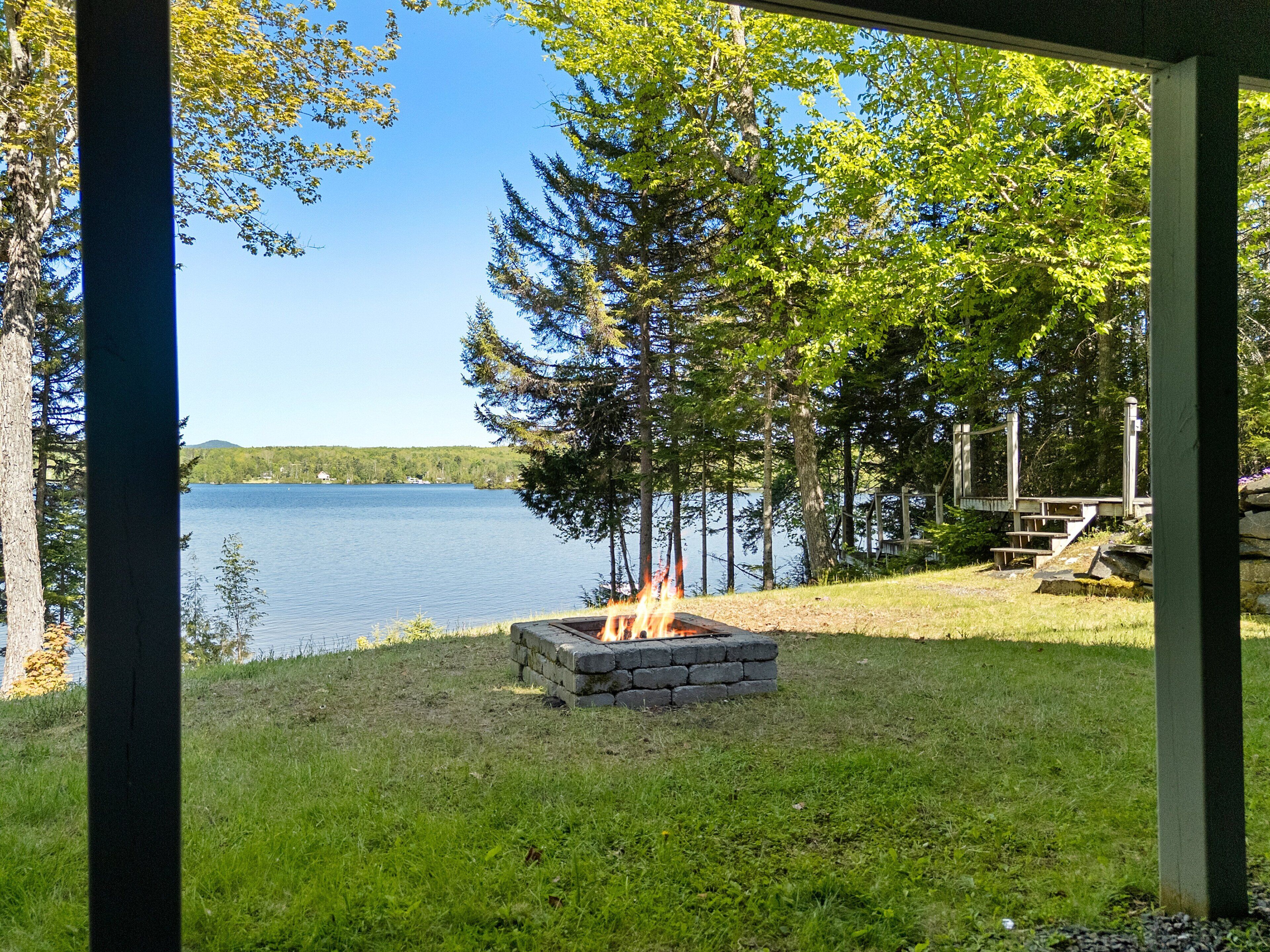 A lakeside view with a fire pit and a wooden deck.