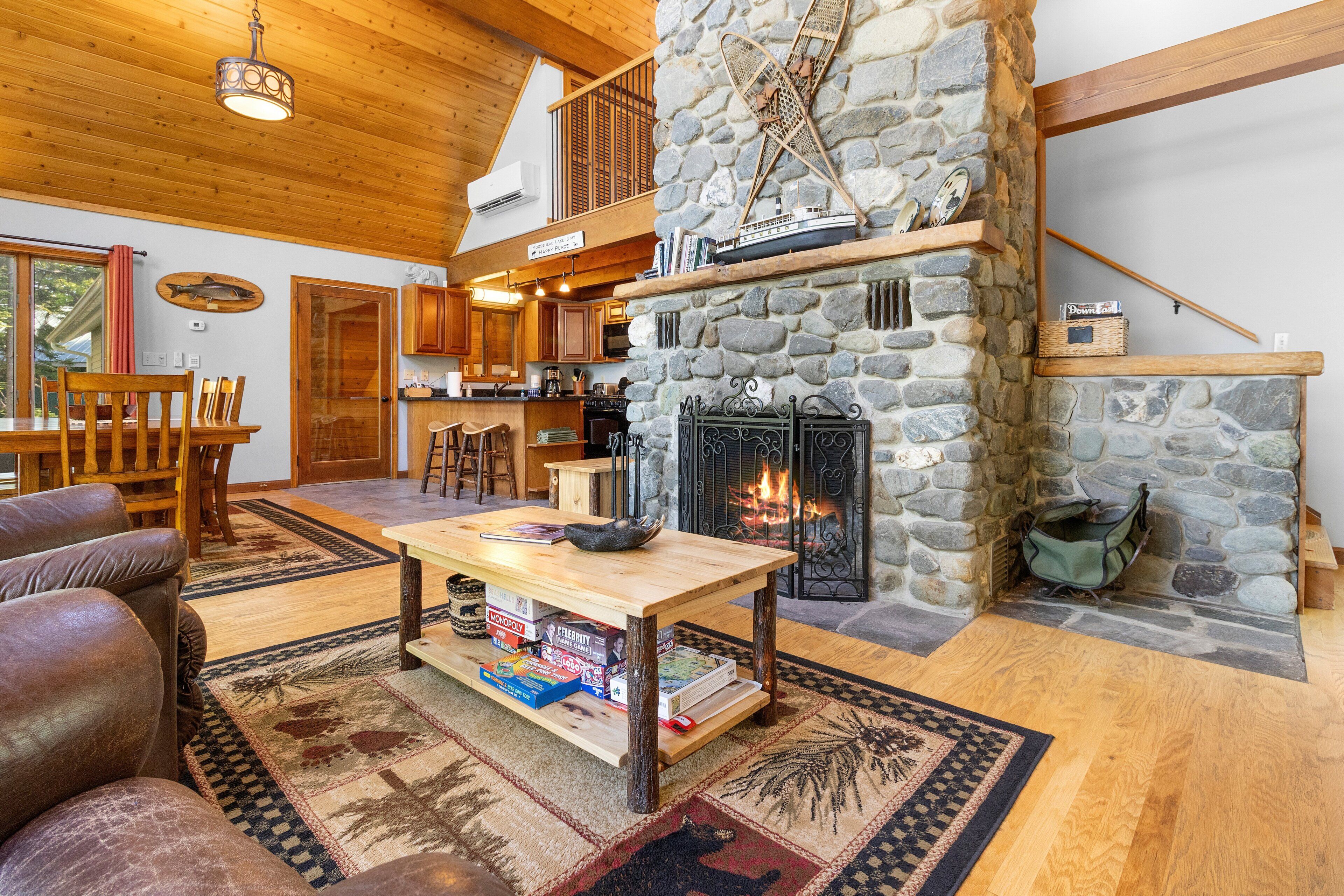A cozy cabin interior with a stone fireplace, wooden furniture, and a dining area.