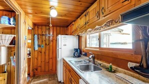 Interior de una cabaña de madera con cocina, que incluye un refrigerador, un lavamanos y una ventana.