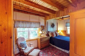 Una habitación con paneles de madera, una cama, un sillón, un aparador y una ventana con cortinas.