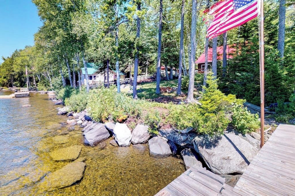 A lakeside cabin with a dock, surrounded by trees and a clear view of the water.