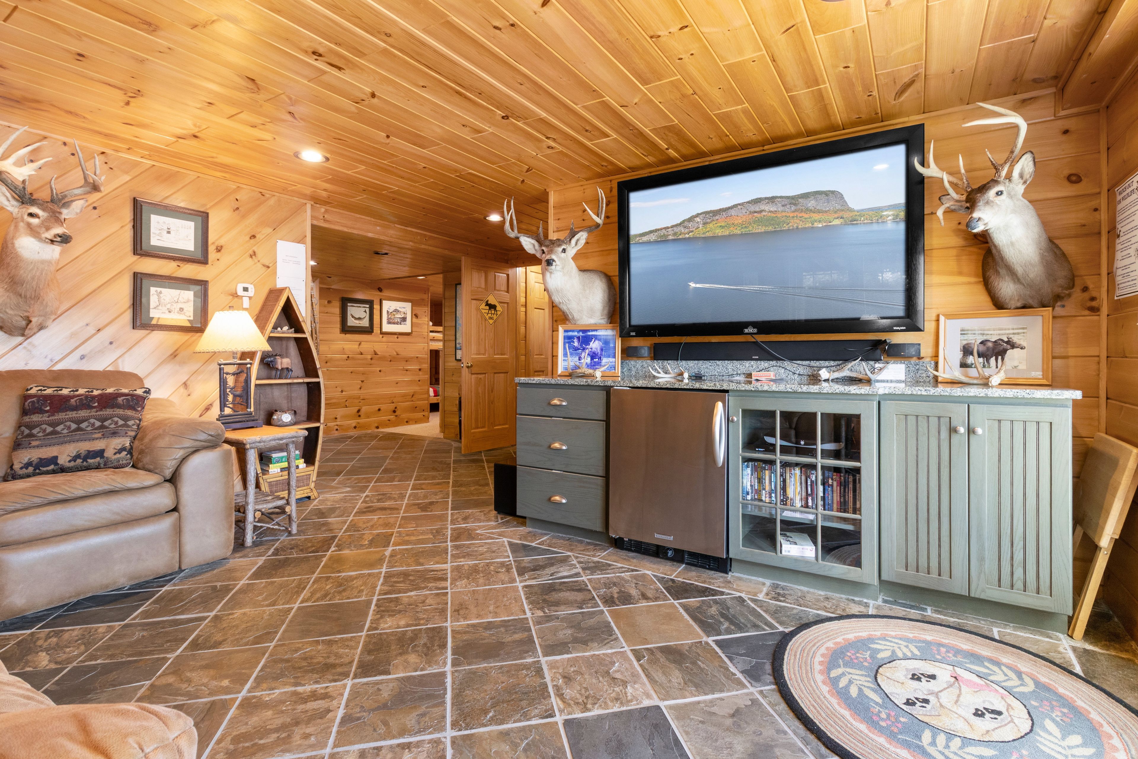 A log cabin interior with a stone-tiled floor, a television mounted on a wall, and antler decorations.