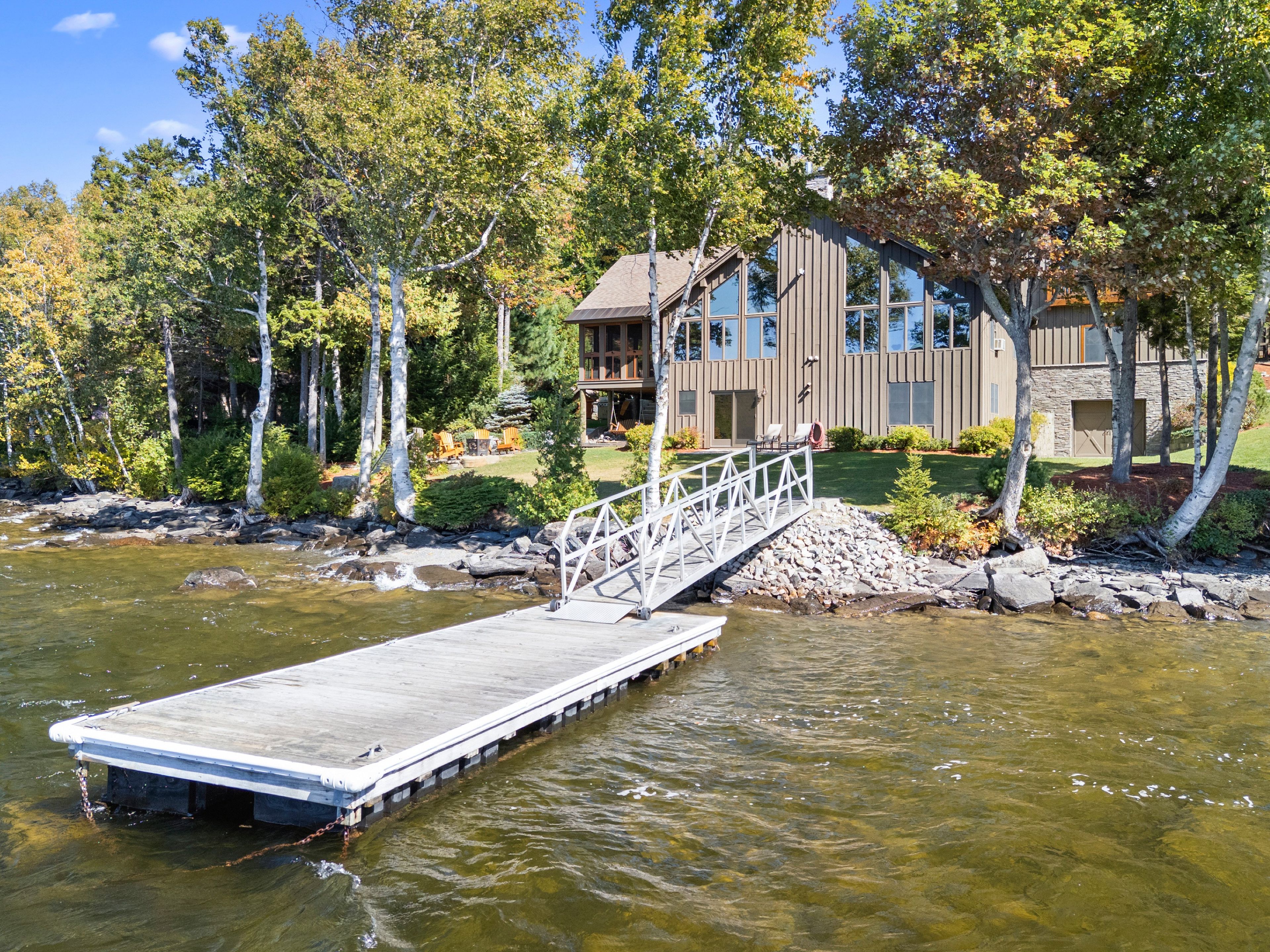 A riverside property with a dock, a wooden bridge, and a modern house with large windows.