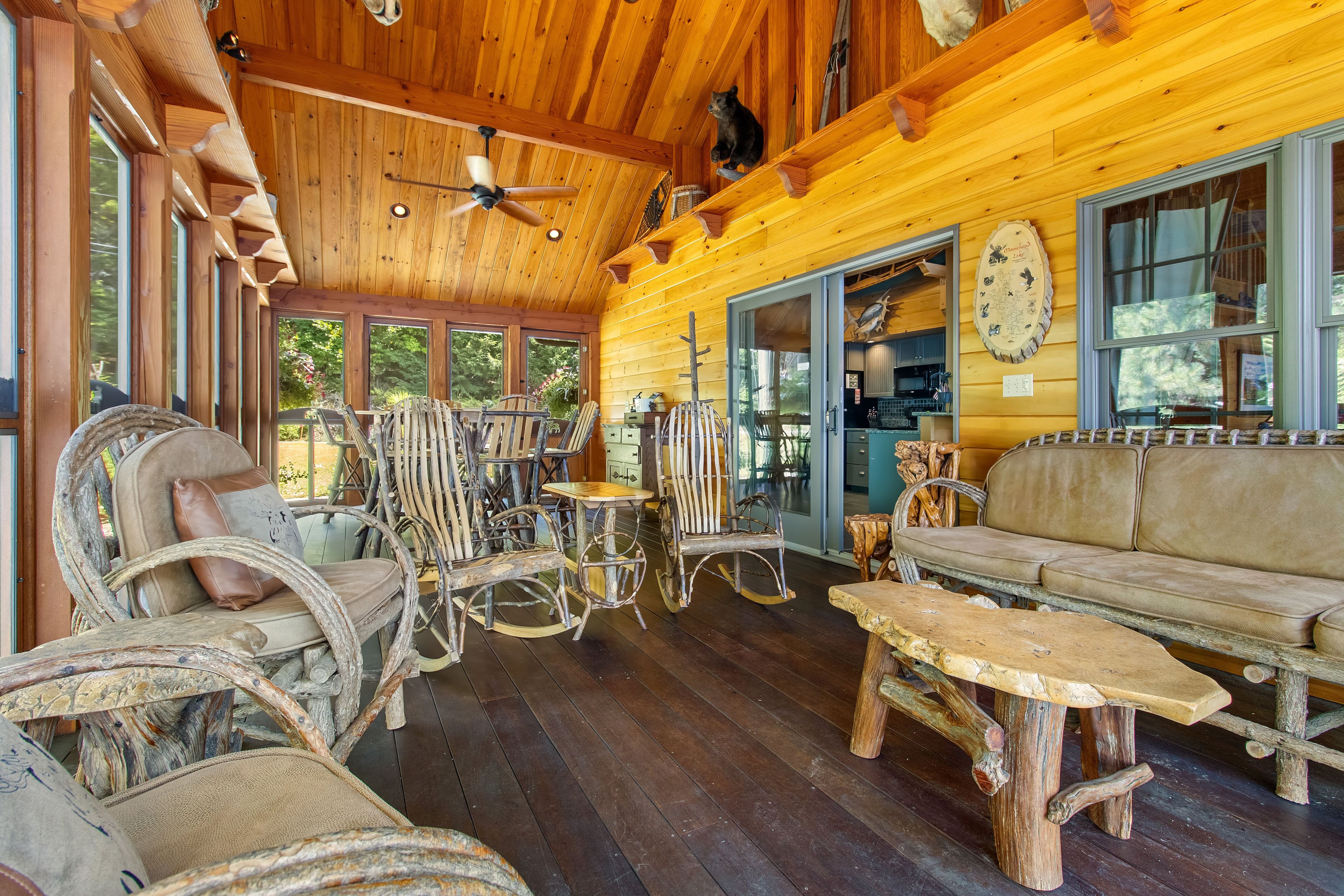 Interior rústico de una cabaña con pisos de madera, un comedor con muebles antiguos y un ventanal con vistas a un bosque.