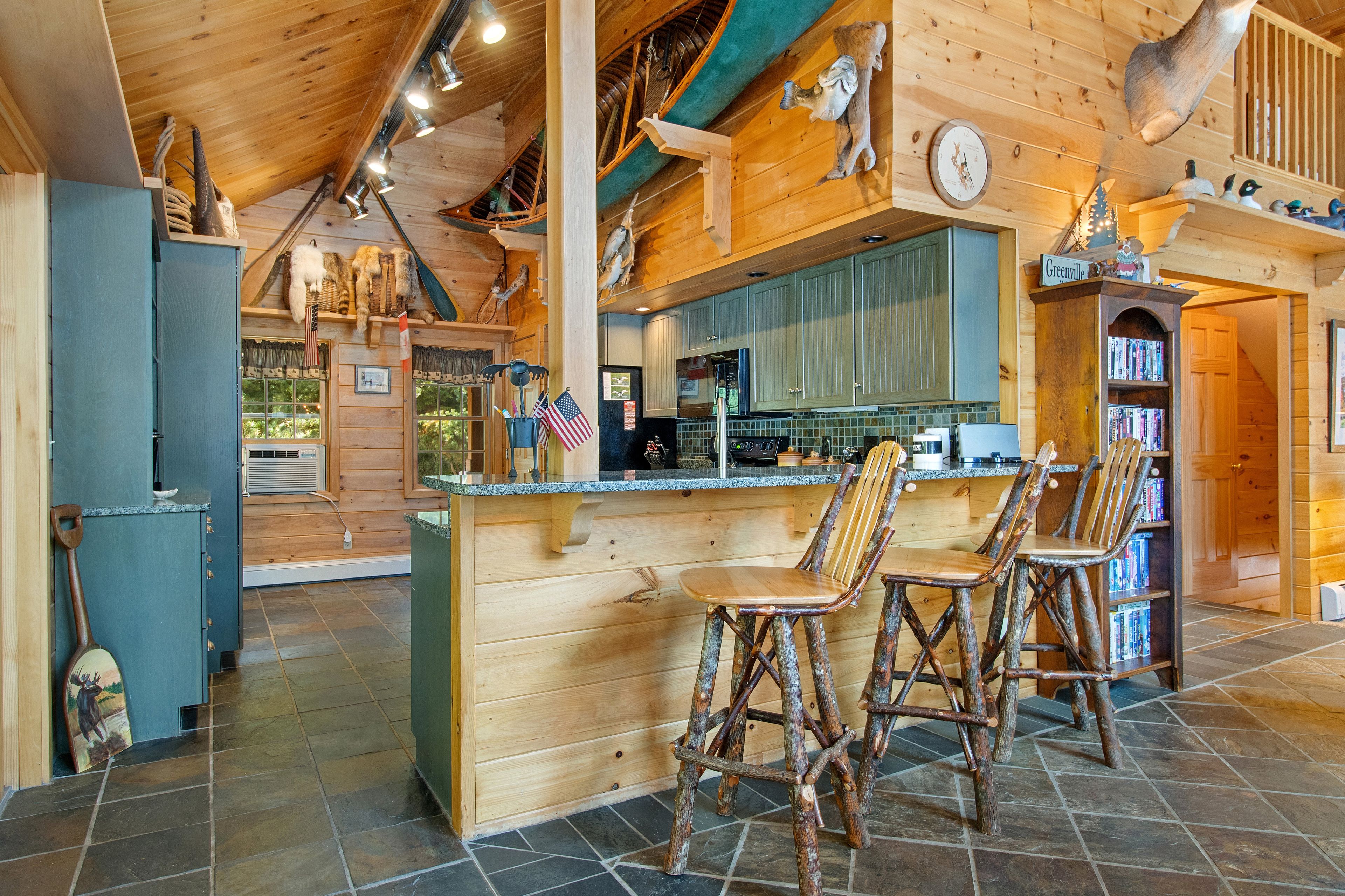 Un interior rústico de madera con una zona de bar, sillas de madera y una cocina con salpicadero de piedra.
