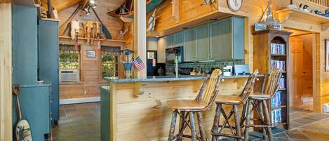 Un interior rústico de madera con una zona de bar, sillas de madera y una cocina con salpicadero de piedra.