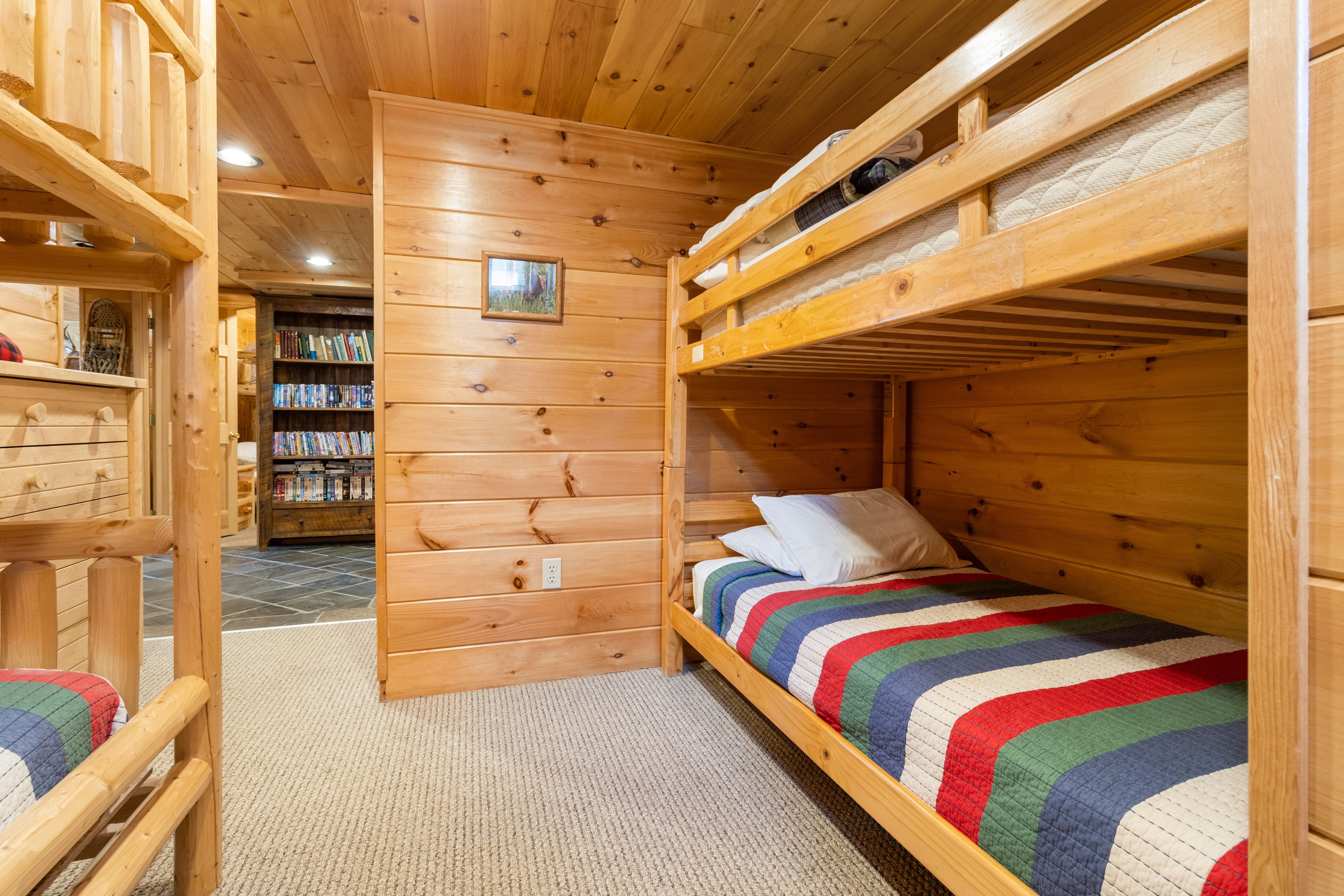 A wooden cabin interior with bunk beds, a bookshelf, and a carpeted floor.