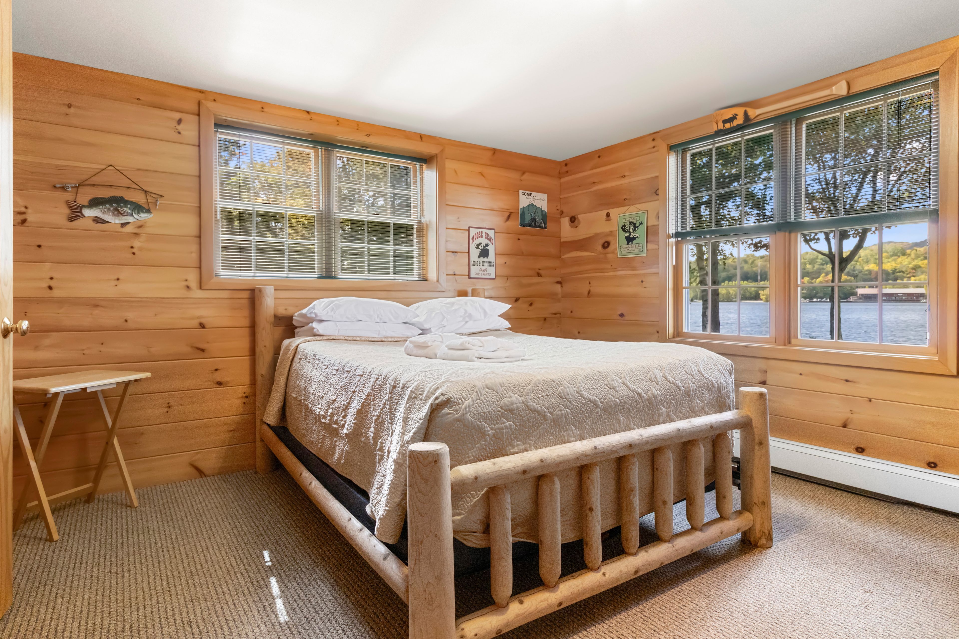 Une pièce de cabane en bois comprenant un lit, deux fenêtres, une petite table et des éléments de décoration murale.