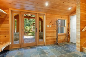 A wooden interior with a stone-tiled floor, wooden doors, and a window with a view of greenery. - Lakeside Lodge with Amazing Water Views, Screened Porch, Dock, & Firepit (Greenville)