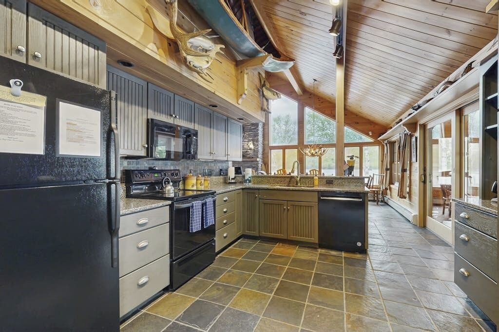Une cuisine avec un sol carrelé en pierre, des meubles de rangement en bois, un réfrigérateur noir et un four à micro-ondes.