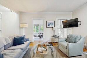 Un salon comprenant un canapé, un fauteuil, une table basse et un téléviseur à écran plat fixé au mur.
