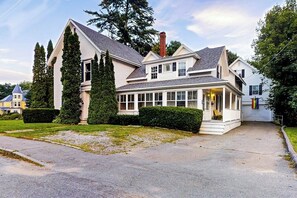 A large, two-story house with a wrap-around porch, a chimney, and a well-maintained lawn.